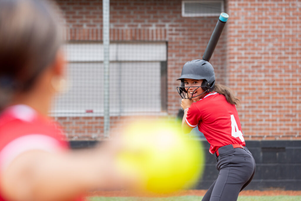 High school softball player batting at a small-town stadium